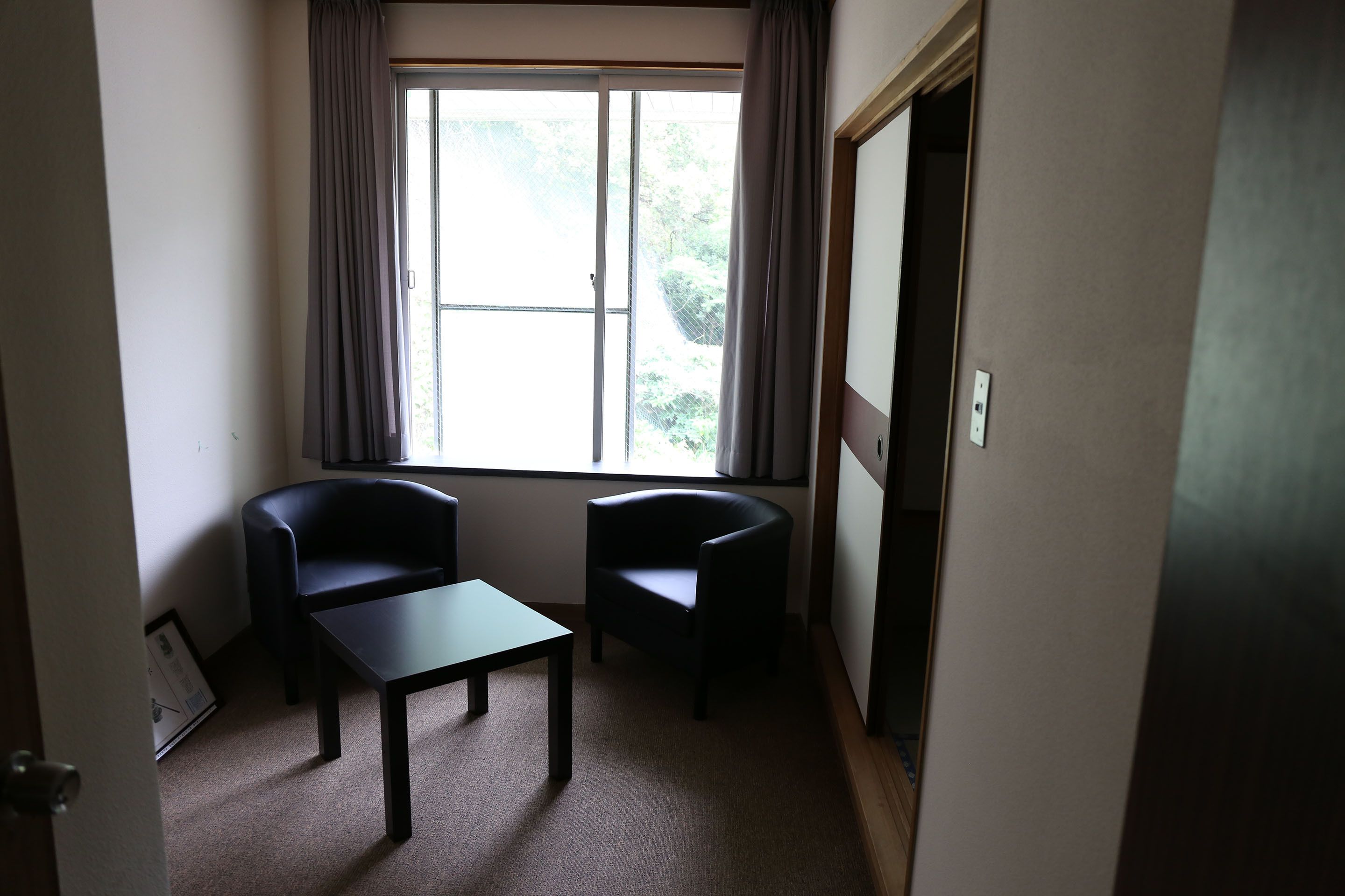 A small room with two chairs, a table, and a window with curtains.