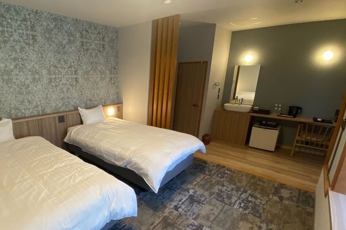 A hotel room with two beds, a bathroom with a sink and mirror, and a small desk with a coffee maker.