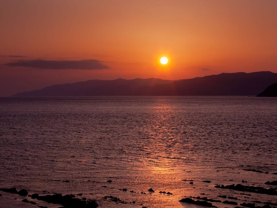 Un atardecer sobre un mar tranquilo con montañas a lo lejos.