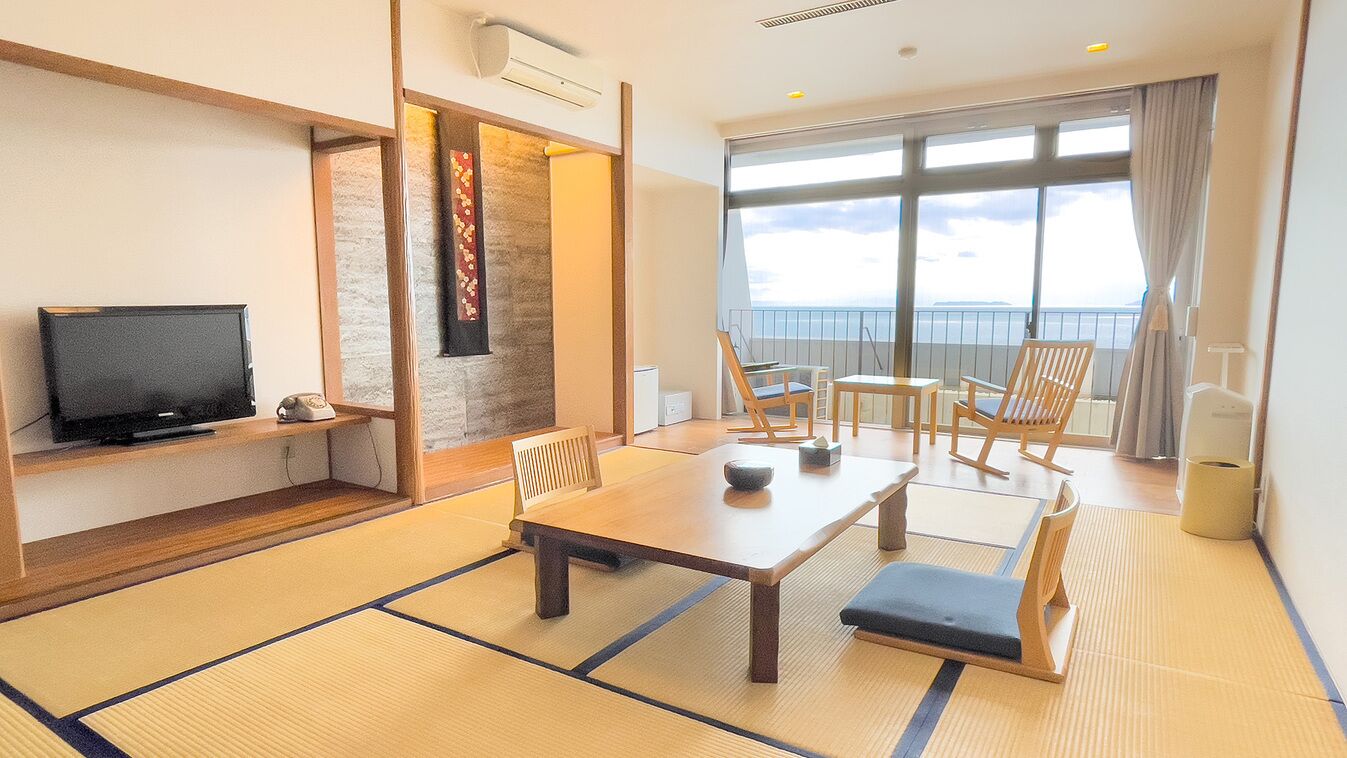 Ein Zimmer mit Tatami-Matten, einem Fernseher, einem Esstisch, Stühlen und Meerblick.