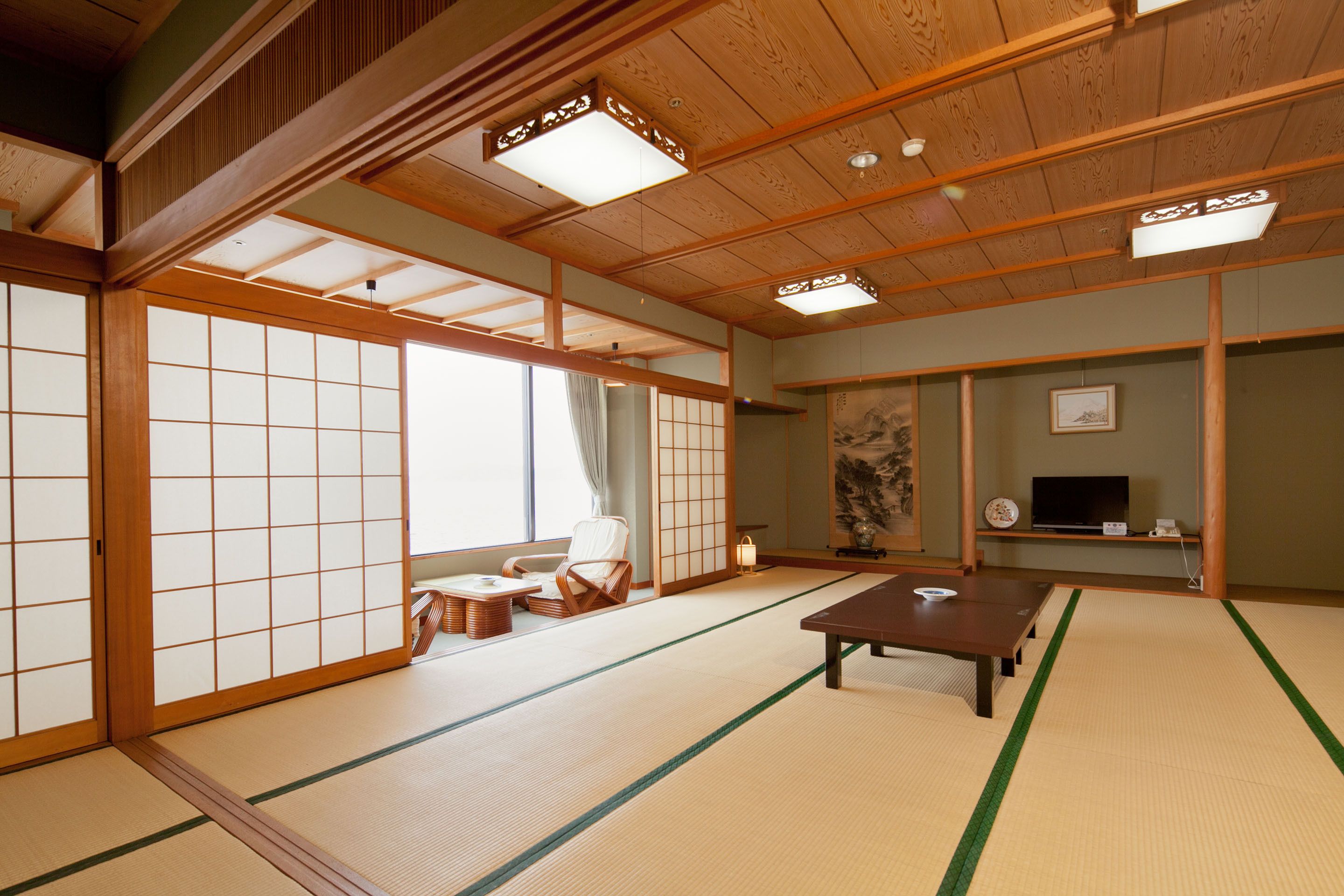 Um quarto japonês tradicional com piso de tatame, portas deslizantes, uma mesa baixa e uma televisão.