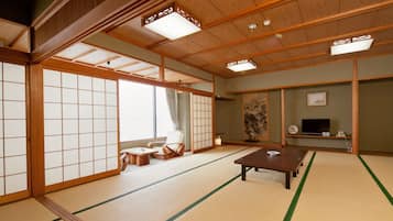 Um quarto japonês tradicional com piso de tatame, portas deslizantes, uma mesa baixa e uma televisão.