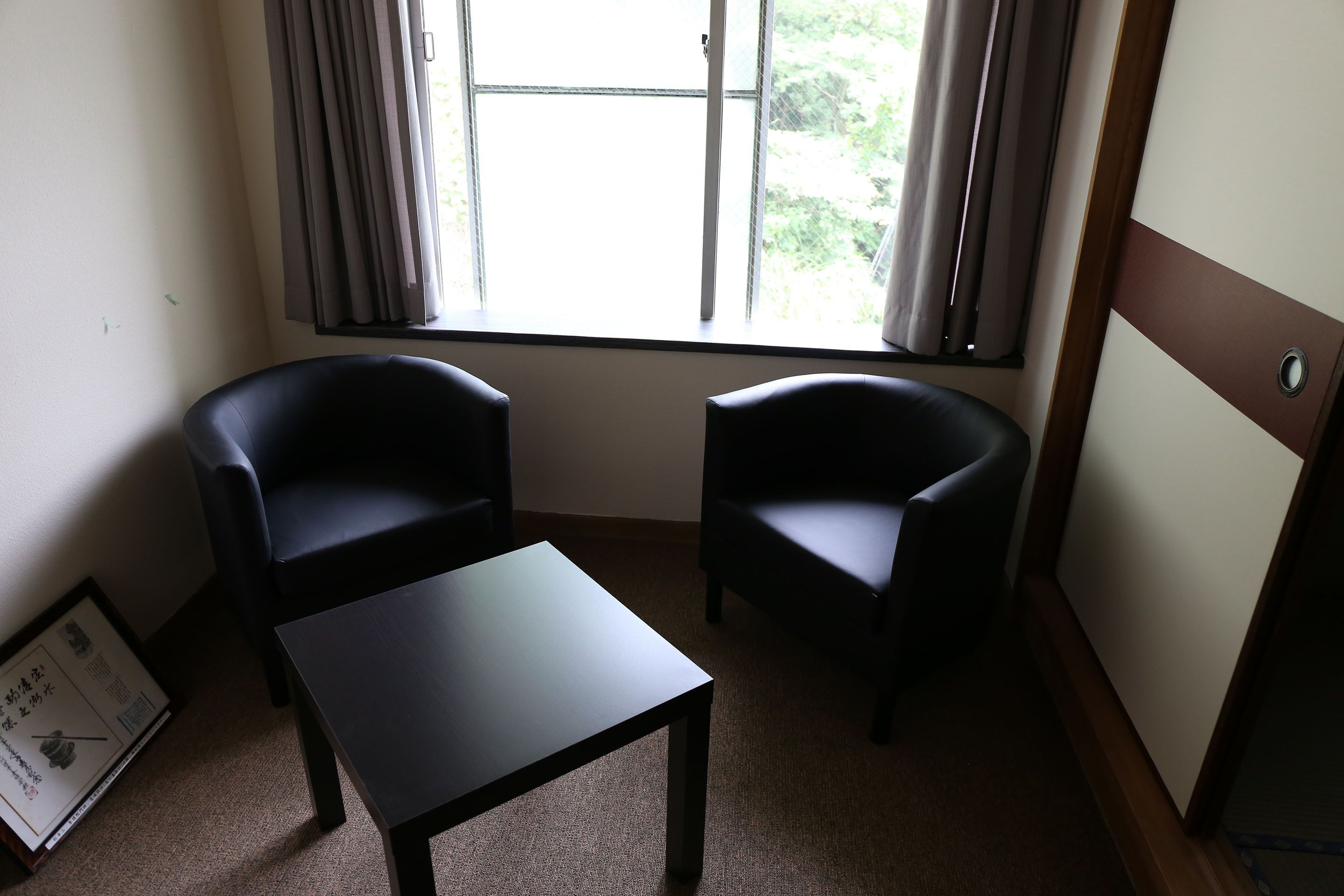 A room with two black armchairs, a small table, and a window with curtains.