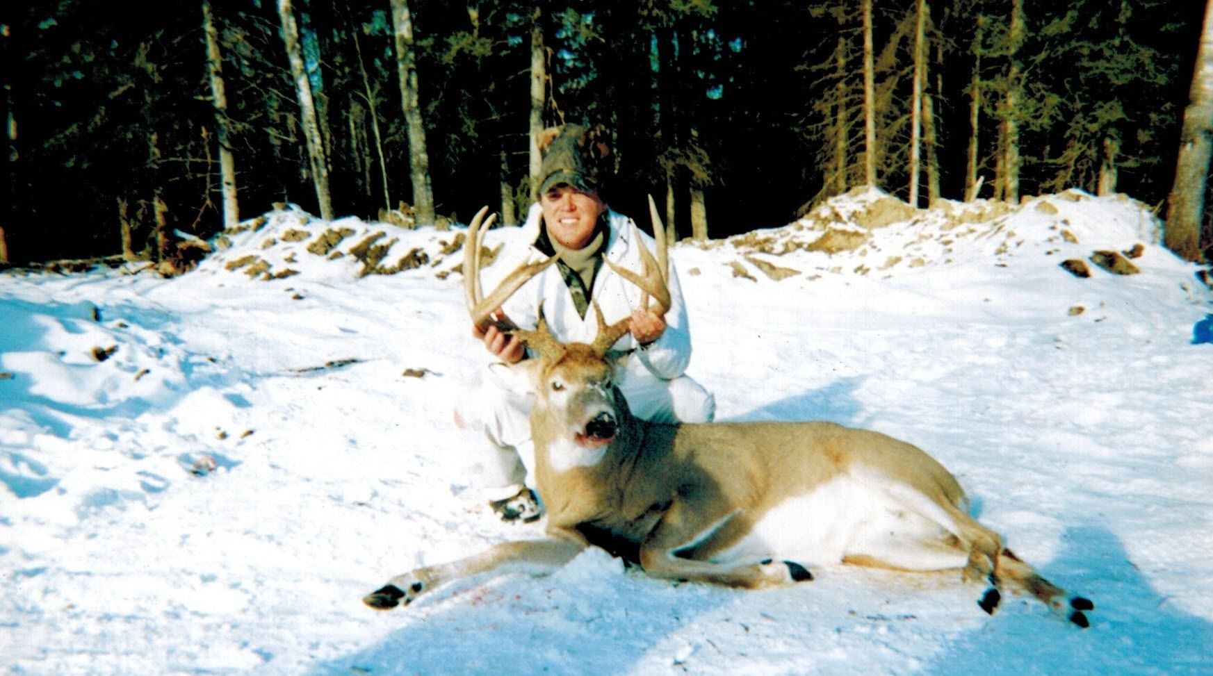 Una persona con un ciervo grande en un bosque nevado.