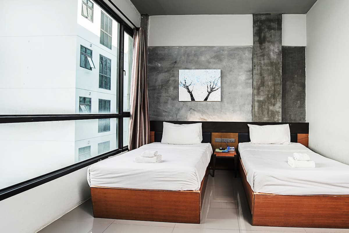 Una habitació d'hotel moderna amb dos llits de fusta, un finestral gran i vista a la ciutat.