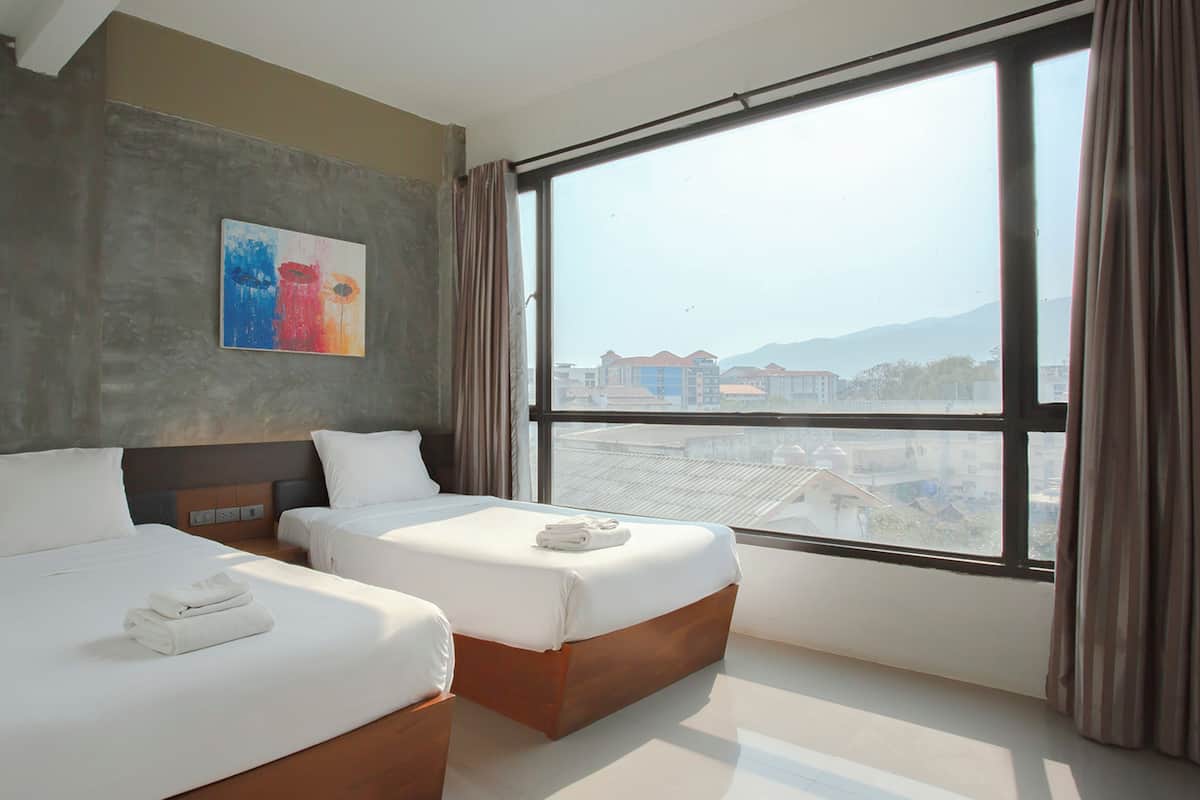 Una habitació d'hotel amb dos llits, una finestra gran amb cortines i un quadre al mur.