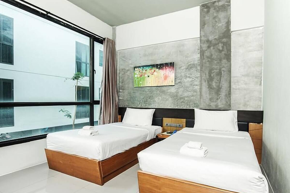 Habitació d'hotel amb dos llits, una finestra gran i un quadre a la paret.