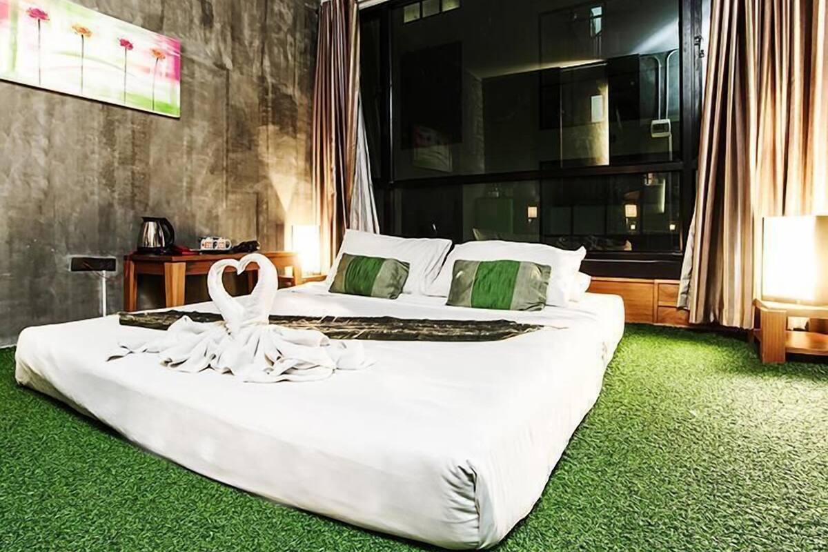 Habitació d'hotel amb llit, gespa artificial verda, un quadre a la paret i una finestra amb cortines.