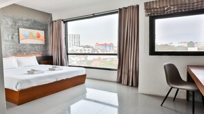 Habitación de hotel moderna con una cama grande, un escritorio y vistas a la ciudad a través de un ventanal amplio.