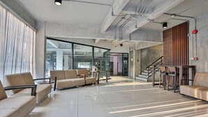 Un hall d’entrée spacieux au design moderne, comprenant un espace détente avec des canapés et des fauteuils, un escalier et de grandes fenêtres laissant entrer la lumière naturelle.