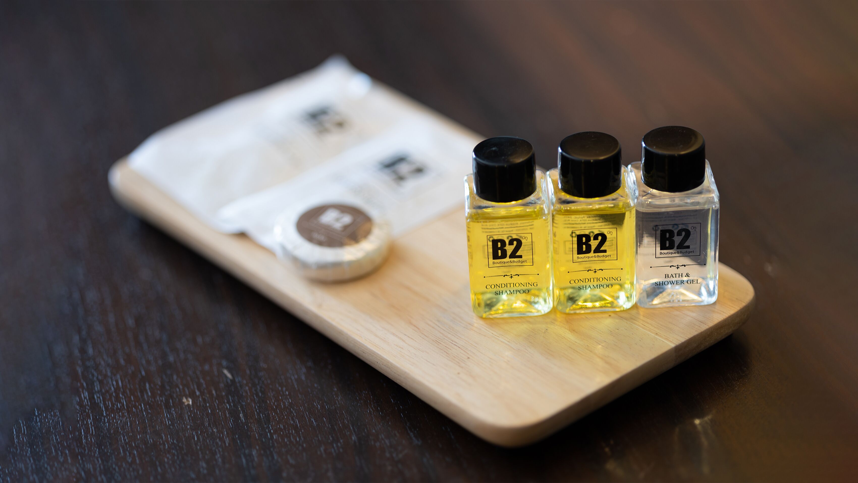 Three bottles of B2 conditioning shampoo and shower gel on a wooden tray.
