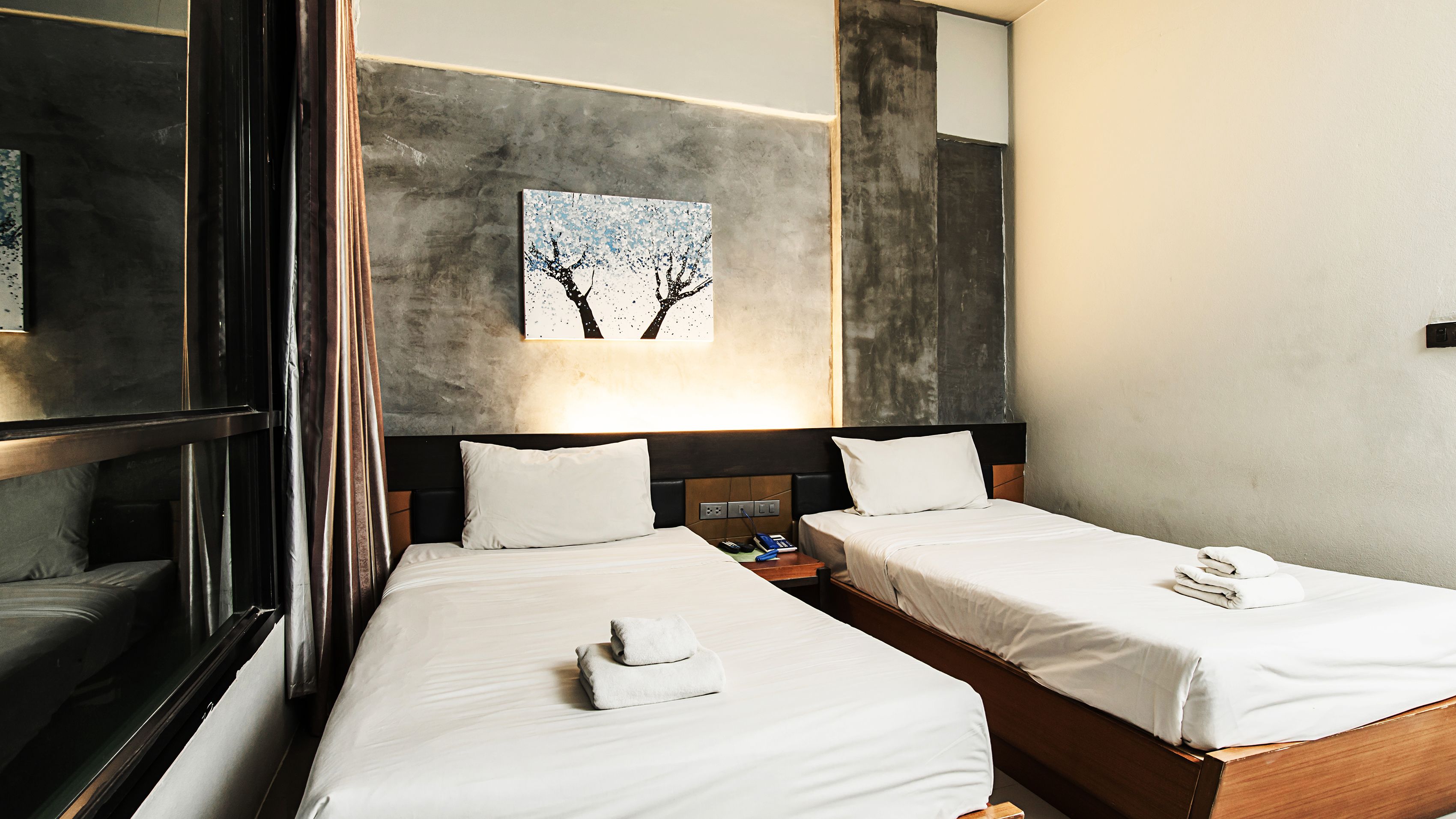 Une chambre d’hôtel avec deux lits, un tableau accroché au mur et un miroir qui reflète la pièce.