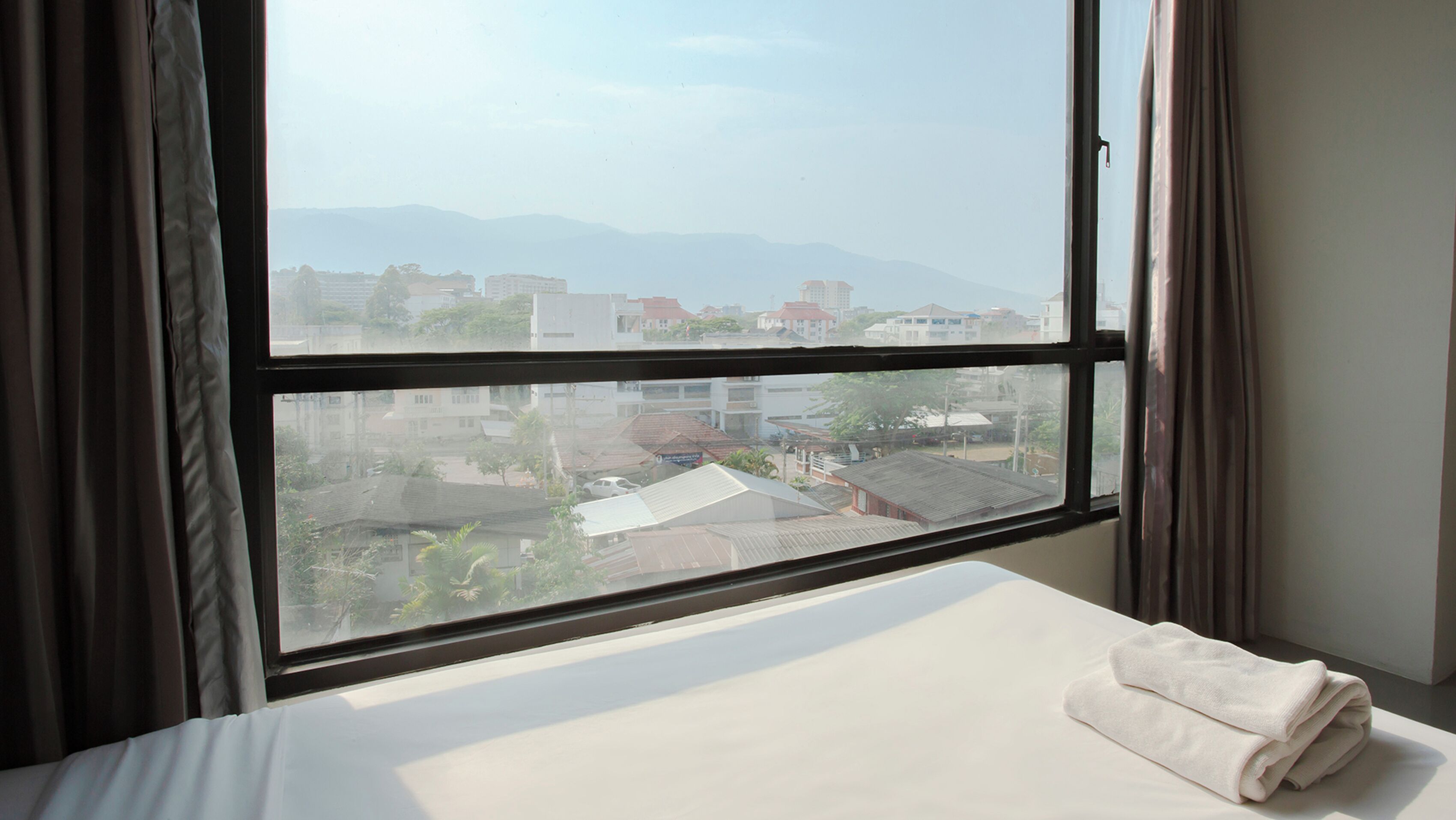 A hotel room with a large window, a neatly made bed, and a view of the cityscape.