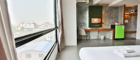 A hotel room with a bed, a desk with a computer, a TV, and a view of buildings outside.