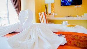 A hotel room with a bed, a television, a window with curtains, and a small table with a cup and a book. - Familyhotel (Khon Kaen)