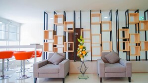 A modern lobby with two grey sofas, a glass coffee table, and orange chairs. A decorative plant is in the center. - Familyhotel (Khon Kaen)