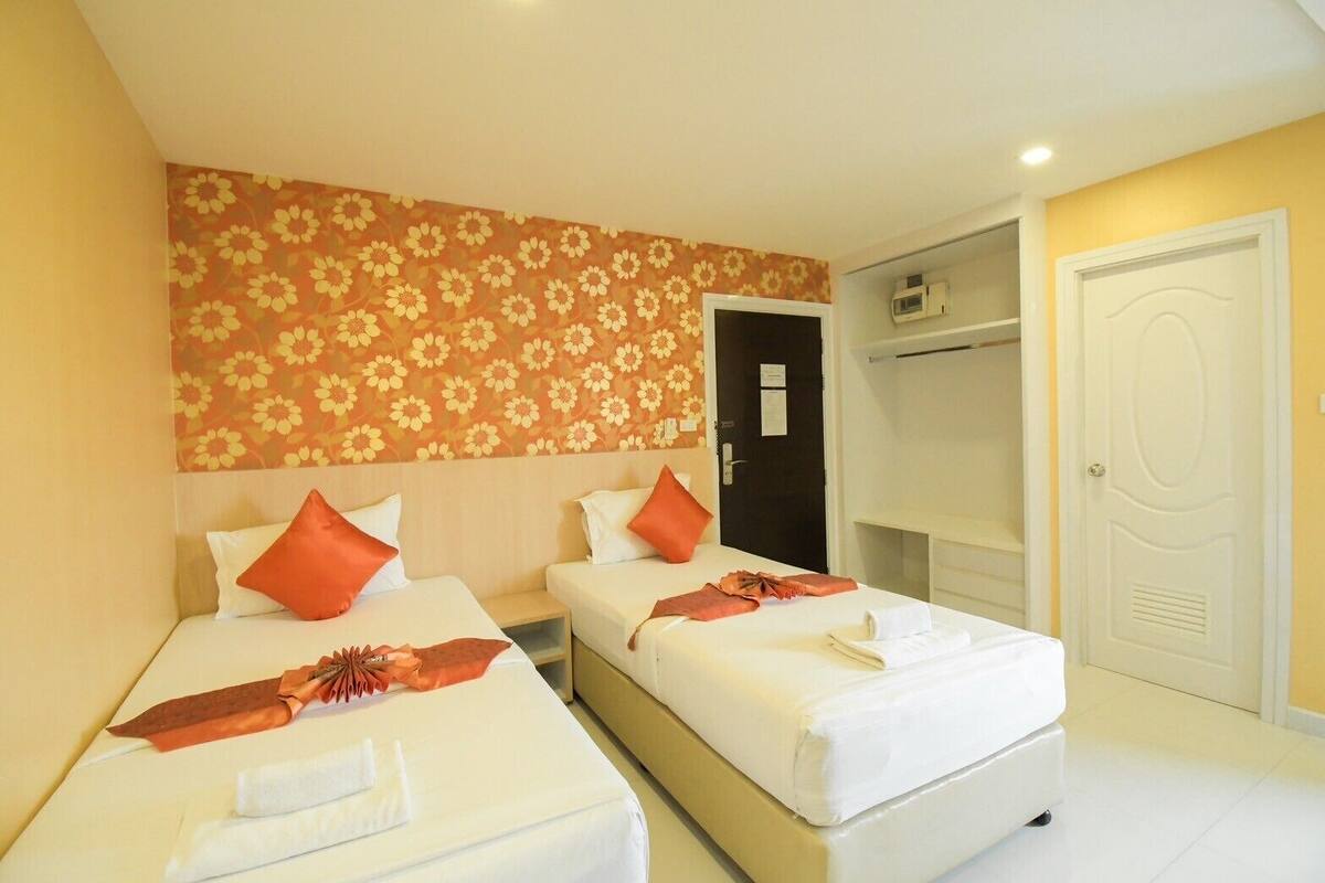 A hotel room with two beds, each with white linens and orange pillows. There is a wardrobe with a mirror and a door to the right.
