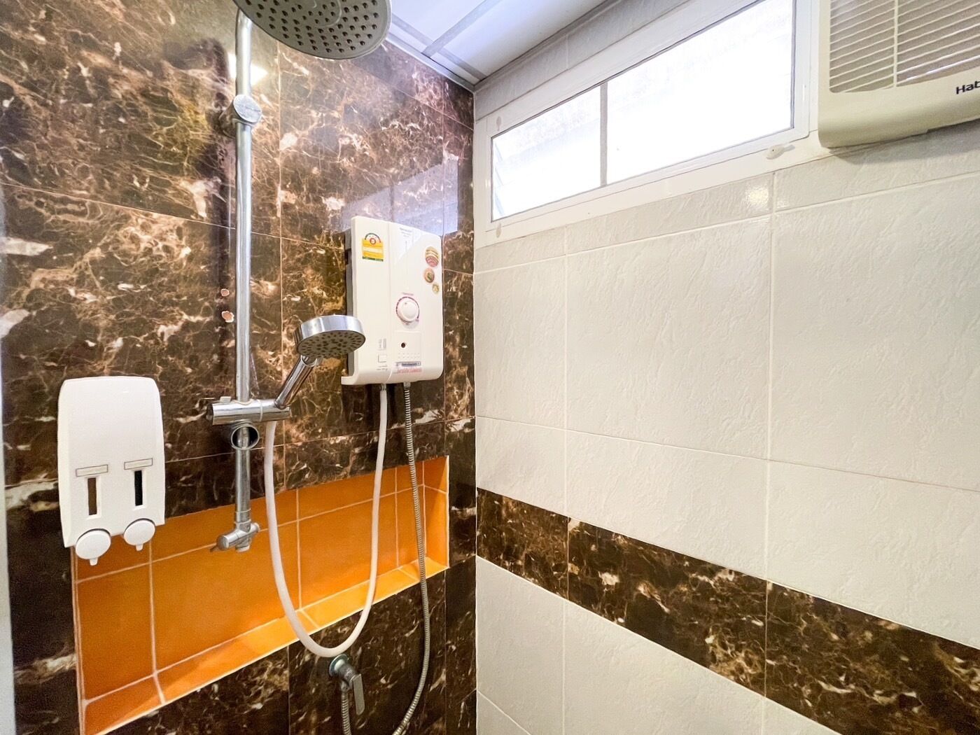 Casa de banho com chuveiro, chuveiro manual, painel de controlo fixado na parede e dispensador de sabonete.
