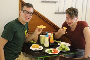 Two people sitting at a table with food, a bottle, and a cup. - Glocal Beachside Hostel (Da Nang)