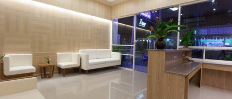 A modern lobby with white sofas, a wooden reception desk, and large windows.