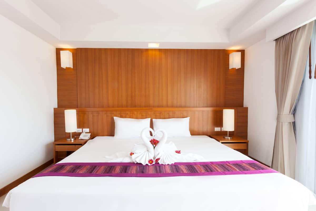 Ein Hotelzimmer mit einem großen Bett, einem Holzkopfteil, Nachttischlampen und Blick ins Freie.