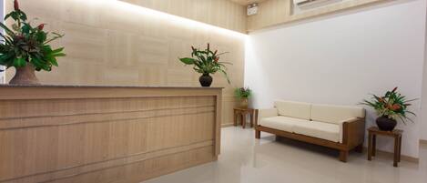 A reception area with a wooden reception desk, a white sofa, and potted plants.