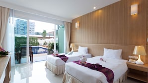 Habitación de hotel con dos camas, cabecera de madera, puerta de vidrio que da a una piscina y una mesita con lámpara.