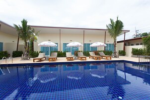A swimming pool with blue tiles, lounge chairs, and umbrellas.
