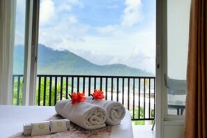 A hotel room with a bed, towels, and a view of a mountainous landscape through a balcony. - Seulawah Grand View (Batu)