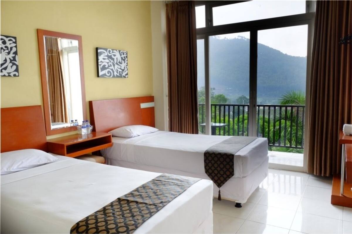A hotel room with two beds, a large window with a view of a mountainous landscape, and a balcony.