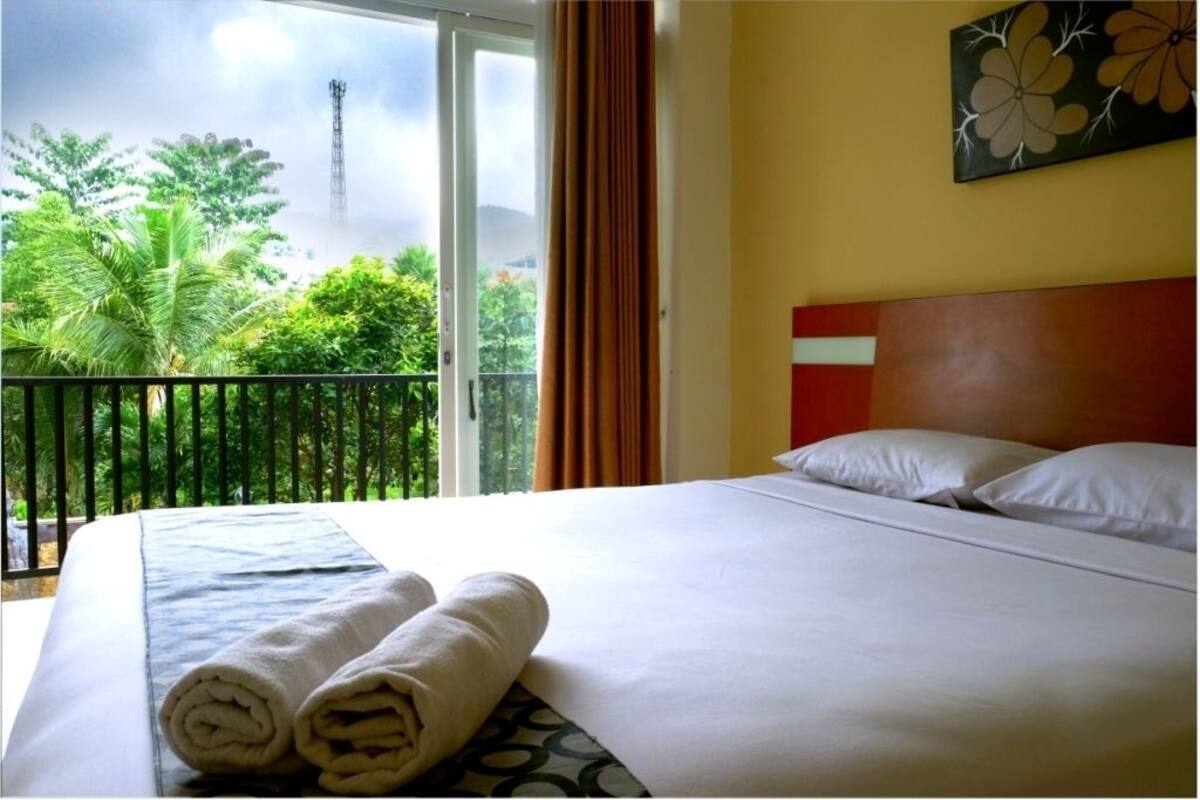 A hotel room with a bed, a view of greenery and a tower outside the window, and a painting on the wall.
