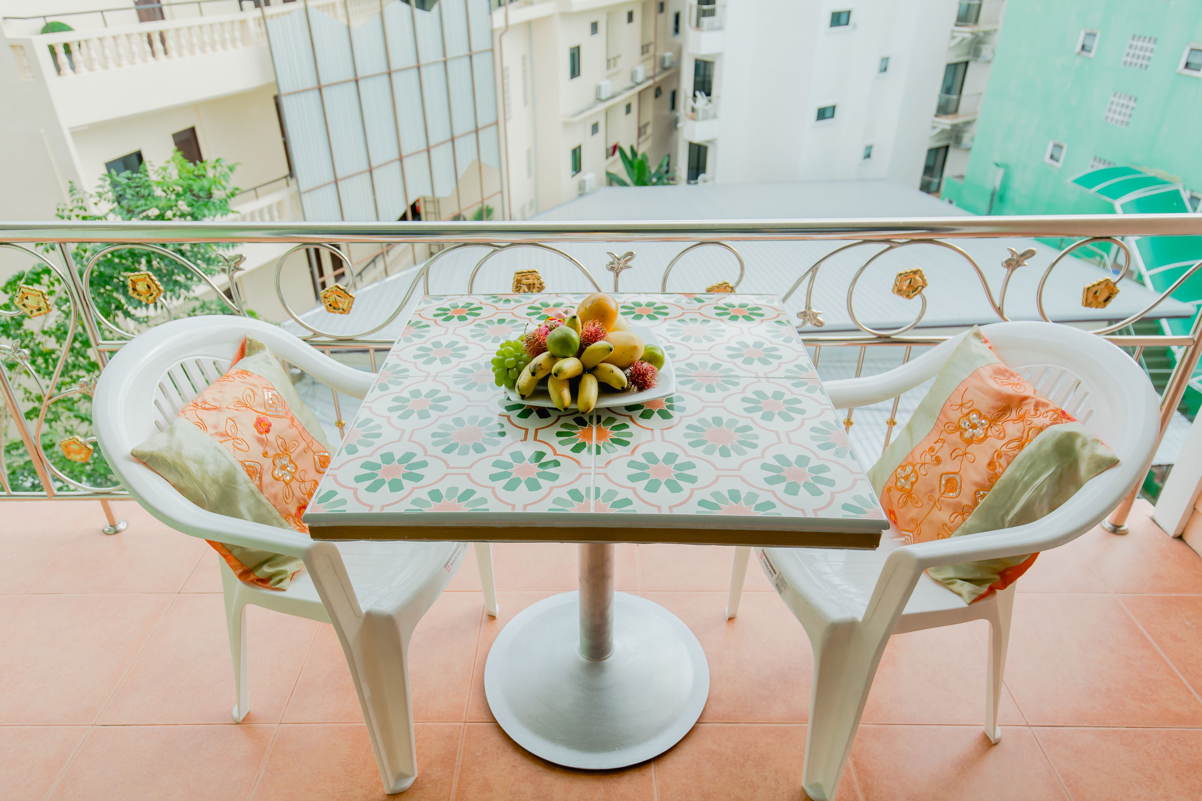 A balcony with a table and chairs, a fruit bowl, and a view of buildings.