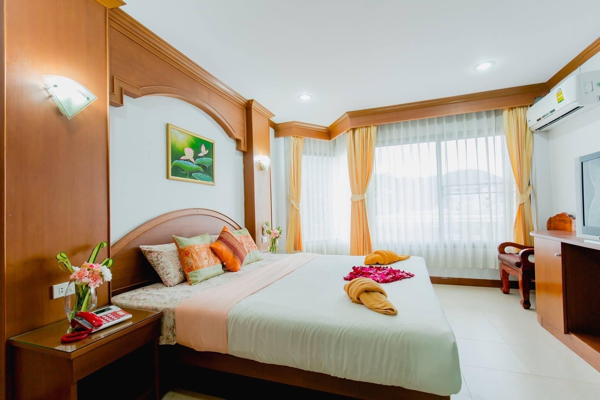 A hotel room with a bed, bedside table, lamp, air conditioning unit, and a television.