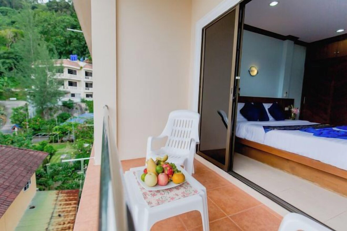 A balcony with a white plastic chair, a table with fruit, and a bed with a blue headboard.