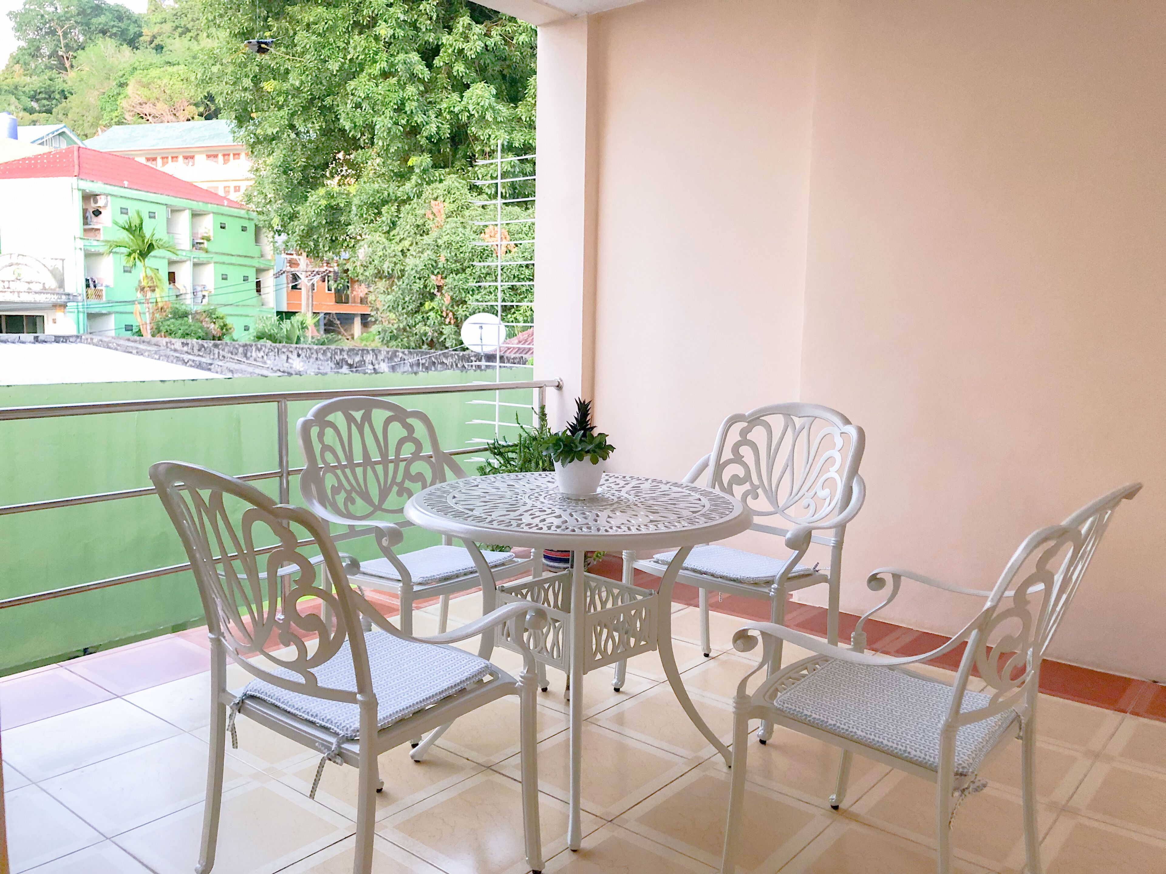 A balcony with a round table and four chairs, a potted plant, and a view of buildings and trees.