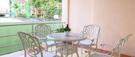 A balcony with a round table and four chairs, a potted plant, and a view of buildings and trees.
