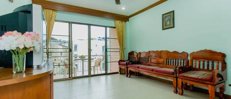 A spacious living area with a wooden sofa, a ceiling fan, and a large window offering a view of the outside.