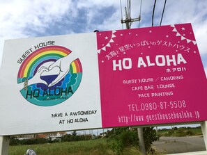 A billboard for HO ALOHA GUEST HOUSE with amenities like a cafe bar, lounge, and face painting. - Guesthouse Ho Aloha - Hostel (Ishigaki)