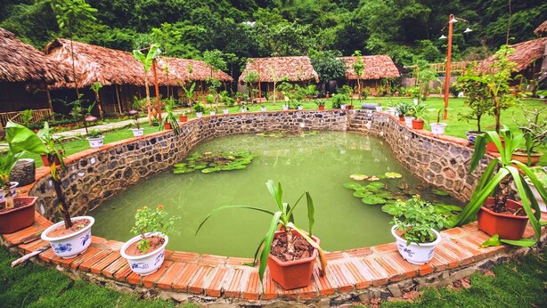 A circular stone pond surrounded by potted plants and thatched-roof structures. - Tam Coc Rice Fields Resort (Nam Hoa Lu)
