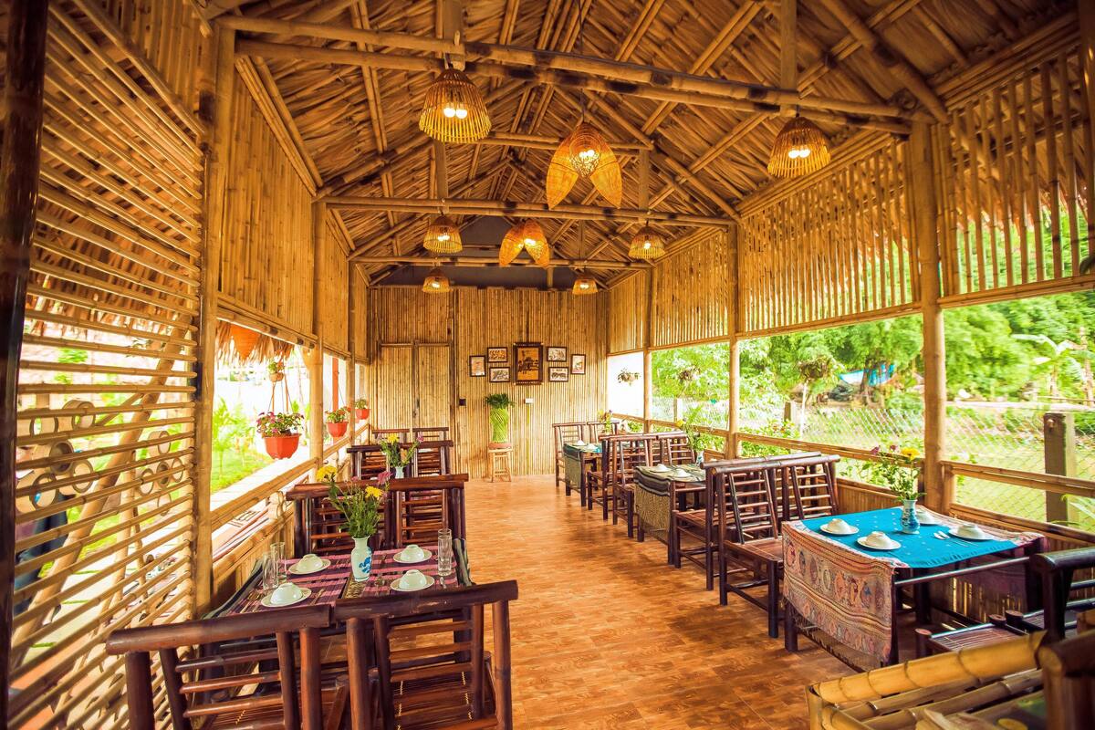 A bamboo-themed restaurant with wooden furniture, hanging light fixtures, and large windows offering a view of greenery.