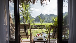 A view from a room with a table and two chairs, overlooking a lush landscape with mountains and a clear sky. - Tam Coc Rice Fields Resort (Nam Hoa Lu)