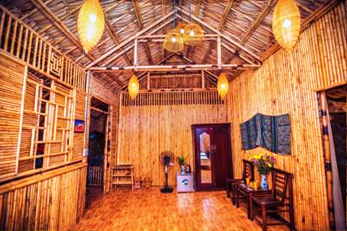 A room with bamboo walls and a high ceiling with exposed beams. There are hanging light fixtures and a door leading to another room.