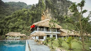 A resort with a swimming pool, thatched-roof structures, and lush greenery. - Tam Coc Rice Fields Resort (Nam Hoa Lu)