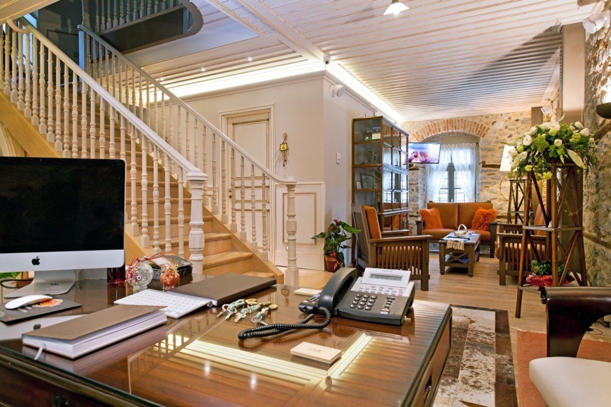 A spacious living area with a wooden staircase, a desk with a computer, a telephone, and a comfortable seating area with cushions.