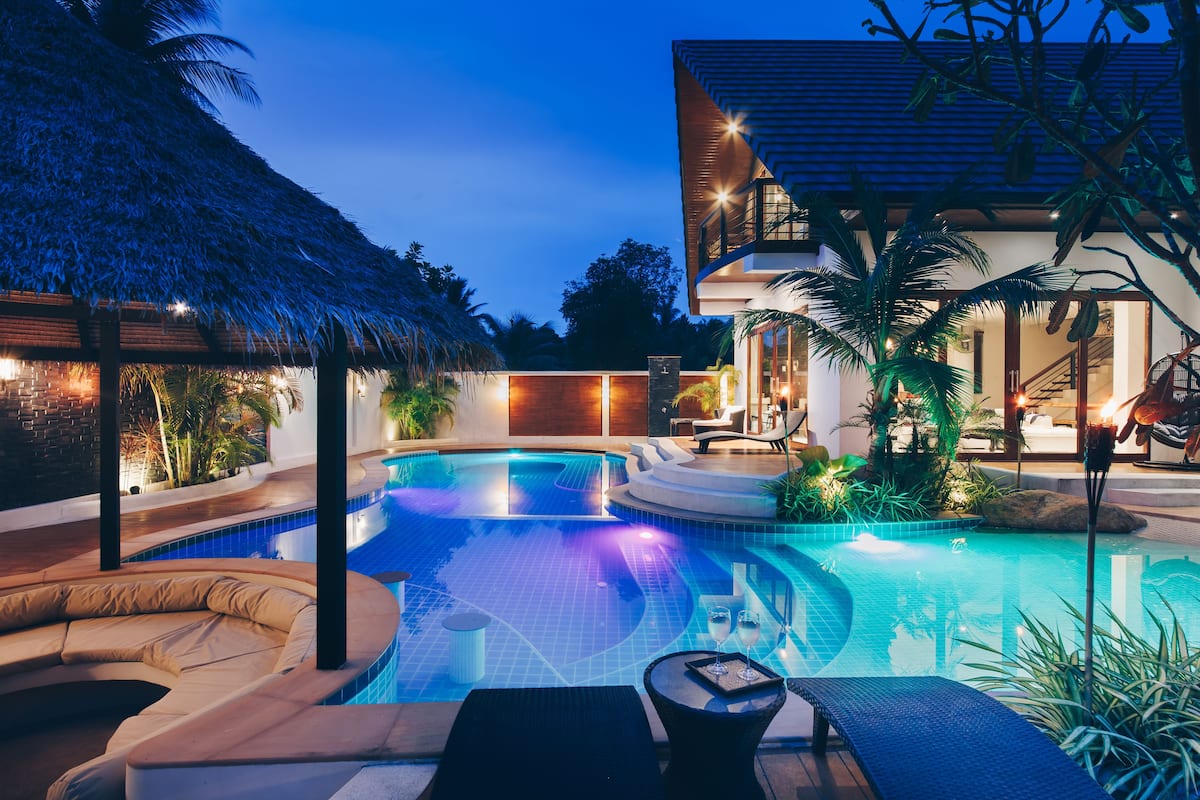 A modern pool area with lounge chairs and a thatched roof structure.
