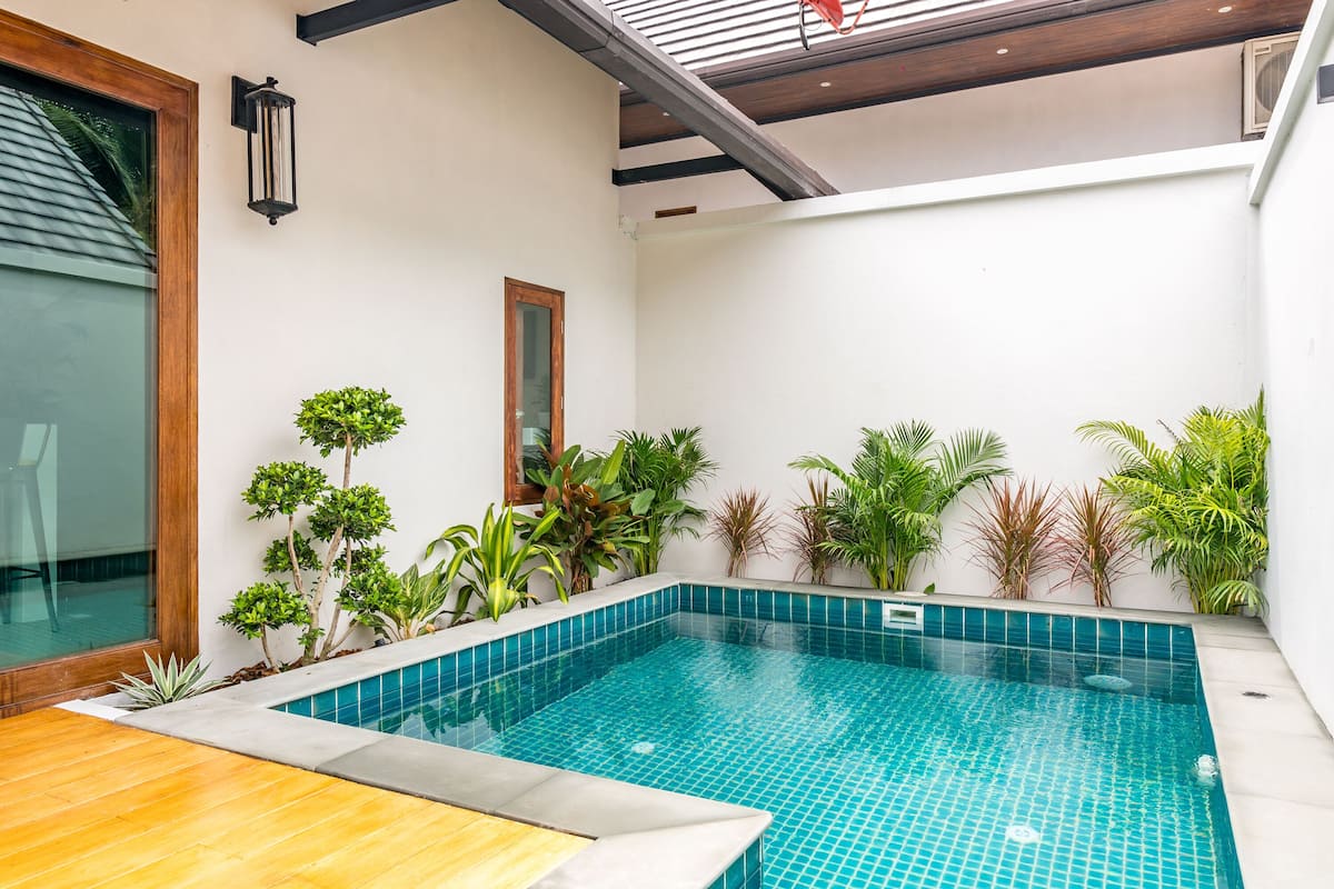 A modern indoor swimming pool with tiled walls, surrounded by various potted plants.