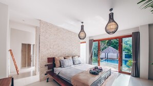 A modern bedroom with a large bed, a brick accent wall, and a view of an outdoor swimming pool. - Coco Lilly Villas (Ko Pha-ngan)