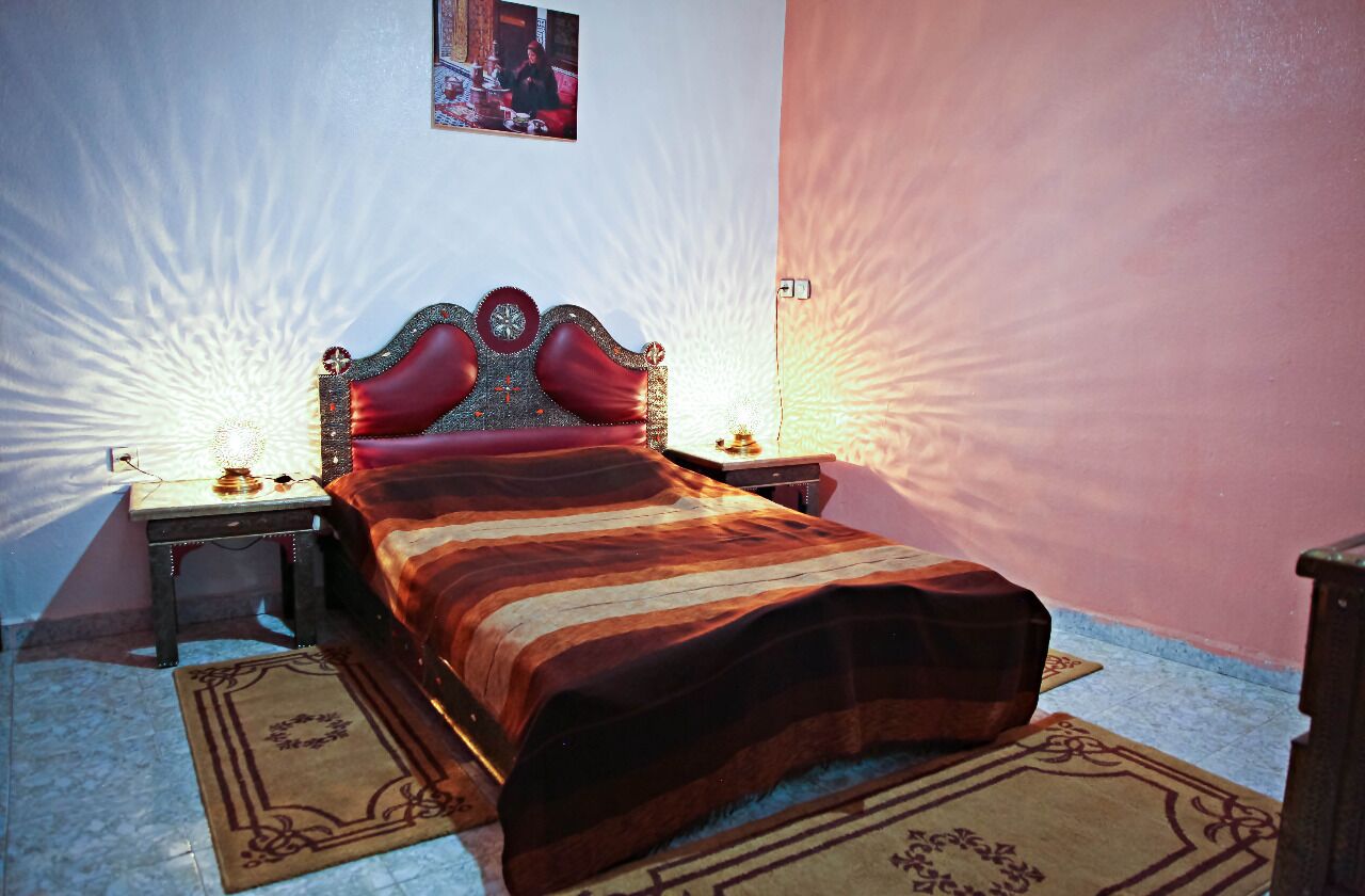 Una cama con una colcha a rayas, dos mesitas de noche con lámparas, un cuadro colgado en la pared y una alfombra estampada.