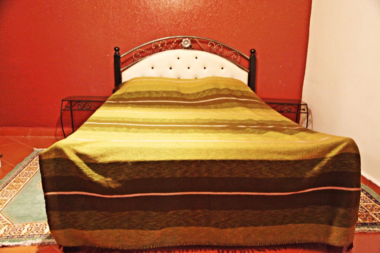 Ein Bett mit einer gestreiften Decke, einem Metall-Kopfstück und einer roten Wand.