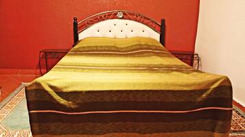 Ein Bett mit einer gestreiften Decke, einem Metall-Kopfstück und einer roten Wand.